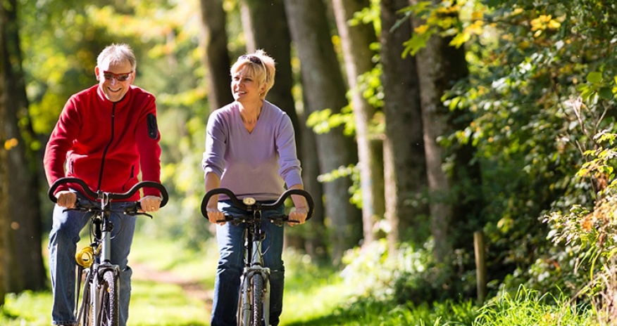 Optimal Aging senior male and female riding a bike through a forest path
