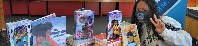 Ainara Alleyne seated beside a pile of HPL books.