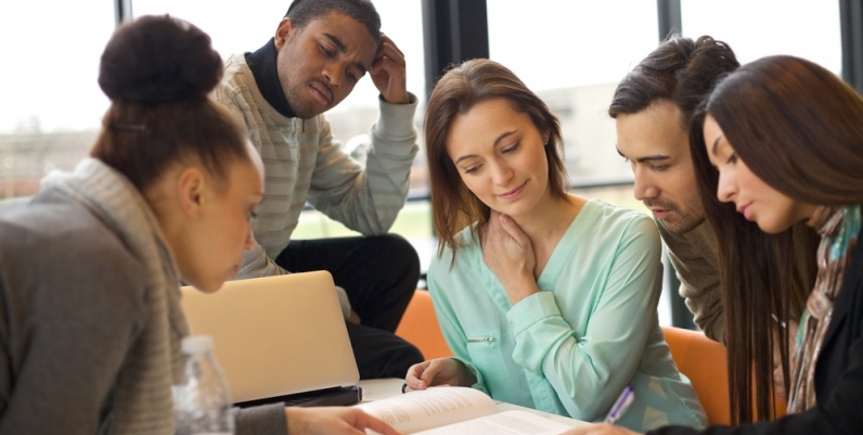 Teens at a table looking at a book Teens at a table looking at a book