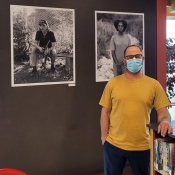 Photographer Niv Shimshon standing infront of two hung photos at the Barton Branch