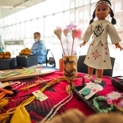 various leather and beadwork items on a black and red blanket covered table, with a doll dressed in white leather native dress