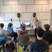 An image of people standing in the sound studio learning about how the equipment works.