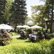 A group of people sitting at small tables under umbrella's listening to a women dressed as a maid at Whitehern