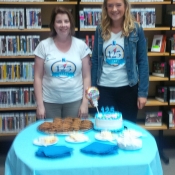 photo of two females in with a table of cake and cookies