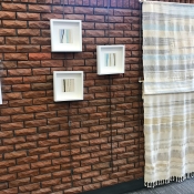 Picture of Emma Enright's Moment Gallery wall at Dundas Branch. 3 white framed photos and a woven blanket hanging on a brown brick wall.