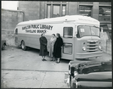Archival photo of three women, including Chief Librarian Freda Waldon, leaning against the Hamilton Public Library Bookmobile, December 4, 1956