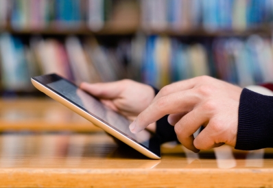 Closeup of hands holding a tablet with books in the background